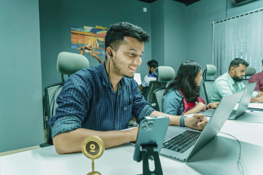 Group of young professionals working together in a modern office setting, using laptops and smartphones.