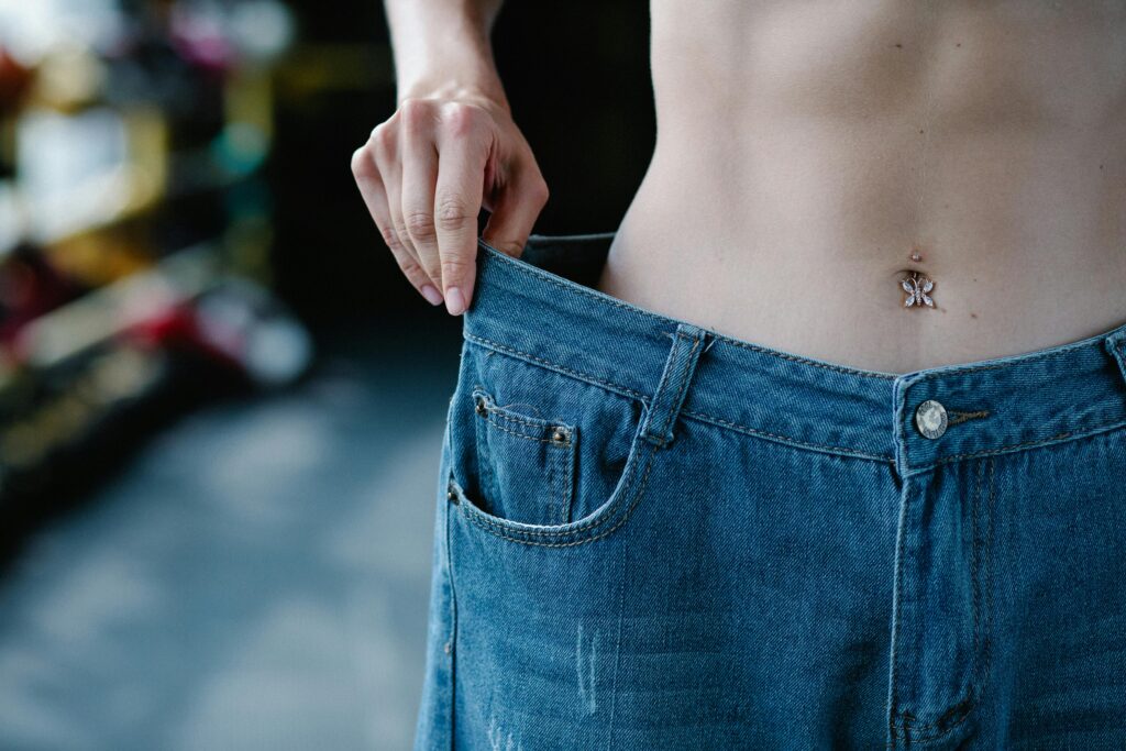 Close-up view of a slim waist and loose jeans representing weight loss or fitness progress.