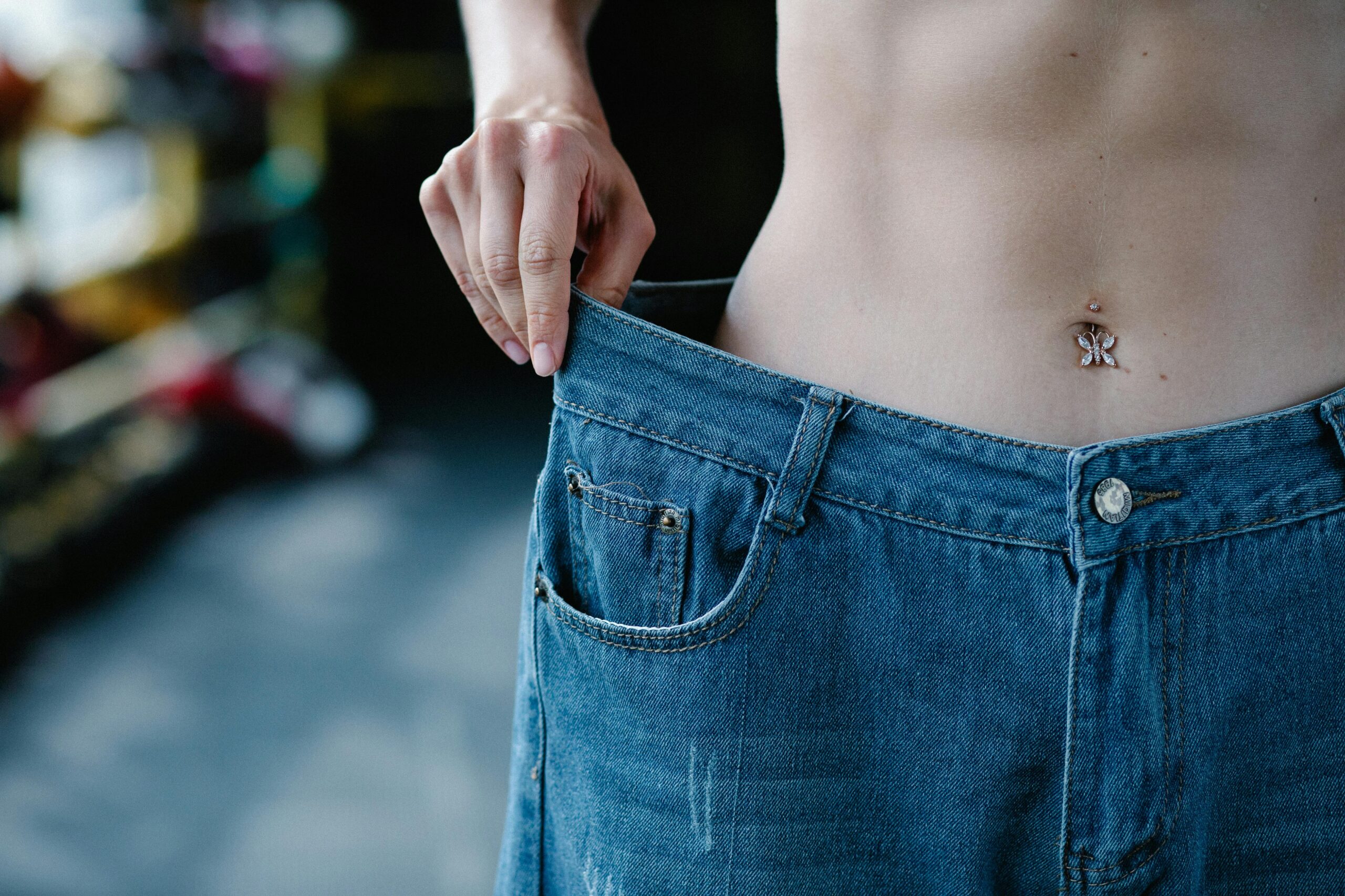Close-up view of a slim waist and loose jeans representing weight loss or fitness progress.