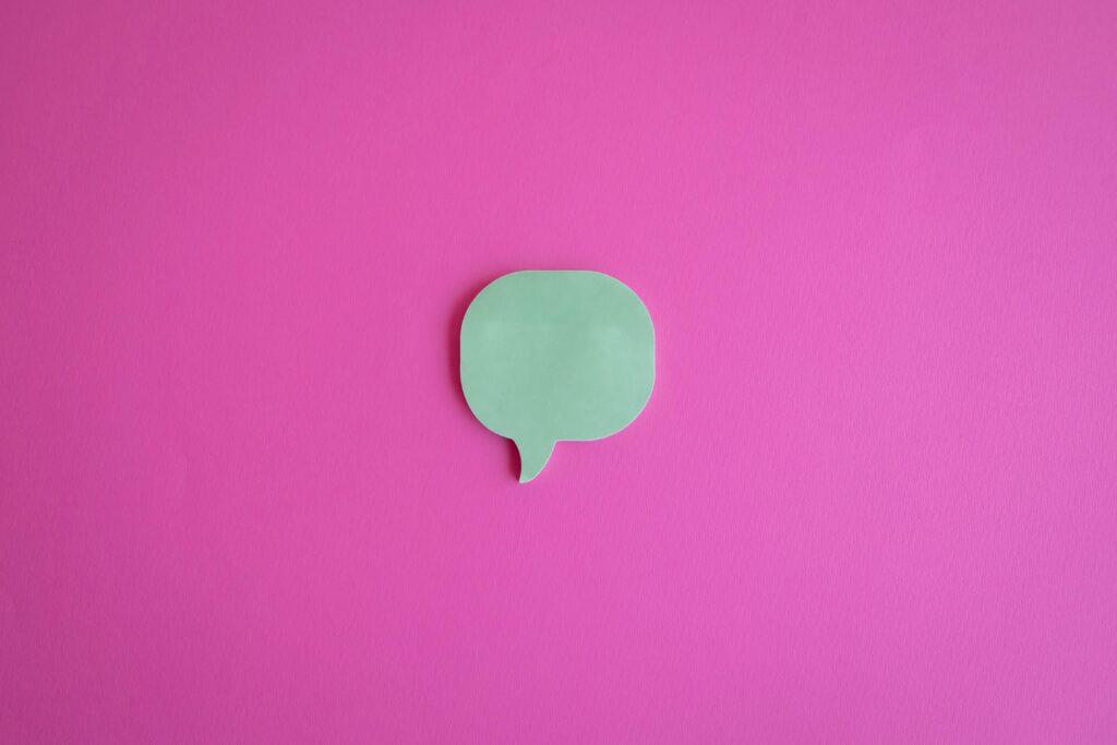 A simple green speech bubble cutout on a vibrant pink background, perfect for creative designs.